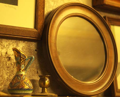 round antique mirror next to an ornamental jug and brass candle stick